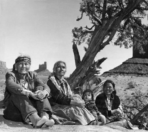 Navajo family sitting on ground by tree. Monument Valley, 1960's.